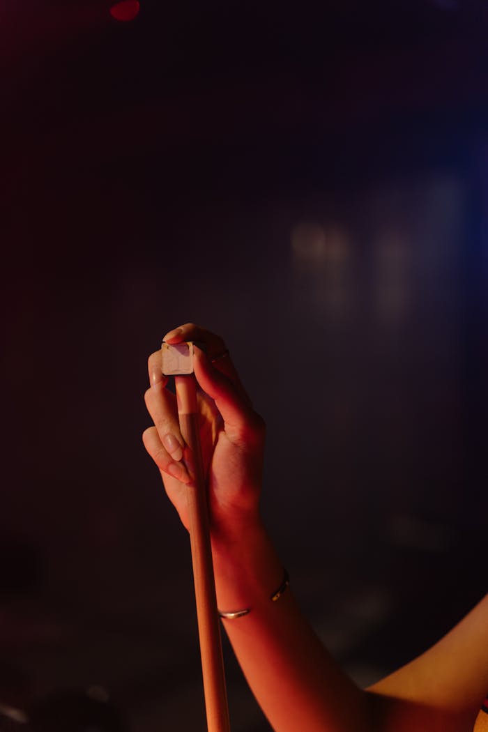 Home Close-up of a hand preparing a pool cue with chalk under moody lighting indoors.